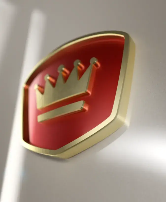 A close-up view of a gold and red emblem featuring a stylized crown design. The emblem has a glossy finish and is set against a blurred metallic background, giving it a sleek and polished appearance.