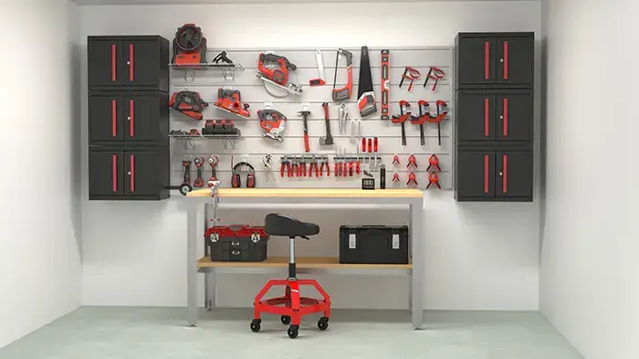 A well-organized home workshop with various tools mounted on a pegboard above a workbench. Tools include hammers, screwdrivers, pliers, and saws, all in red and black. Below the workbench are two toolboxes and a black and red rolling stool. Black cabinets are mounted on both sides of the pegboard.