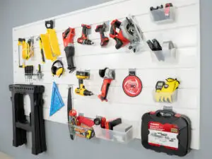 A wall-mounted tool organizer holds various tools including a circular saw, drills, measuring tape, safety gloves, ear protection, screwdrivers, and a toolbox. There are multiple shelves and hooks to neatly arrange the equipment for easy access and storage.