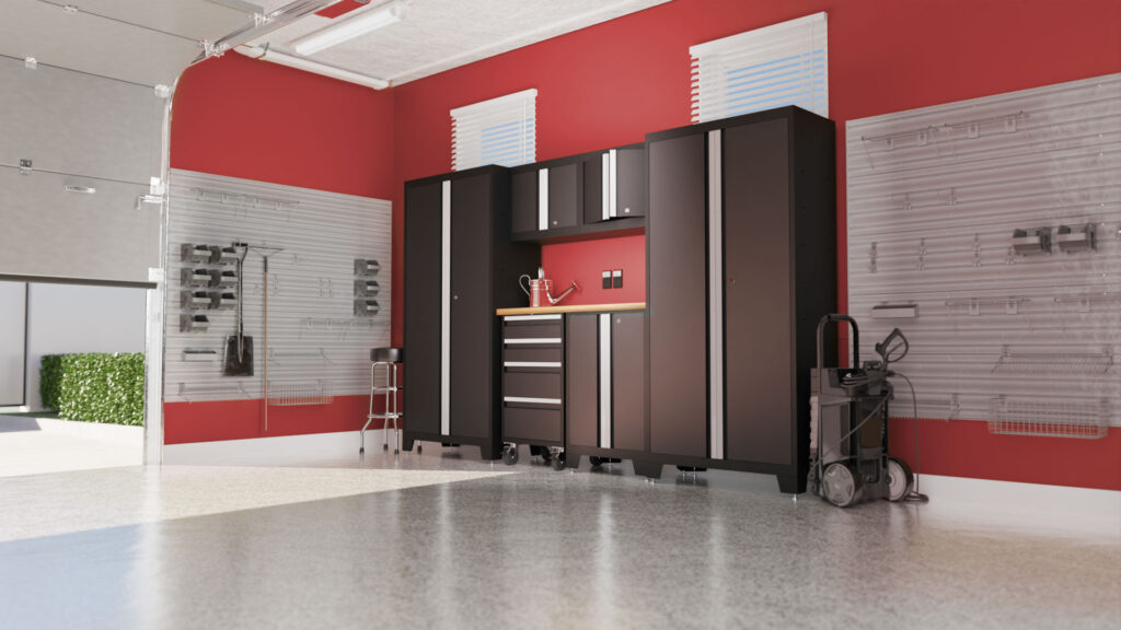 A neat garage with red walls featuring a set of sleek black cabinets and drawers. The workspace is organized, with overhead lighting, slat walls for storage, and a clear, glossy floor. A small window allows natural light to enter.