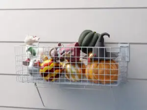 A metal wire basket mounted on a wall keeps your space clutter-free, filled with decorative pumpkins, a pumpkin with a witch hat, and various autumn and Halloween-themed ornaments.
