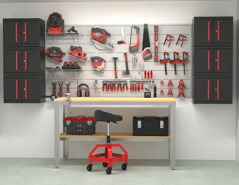 A neatly organized workshop featuring black and red garage cabinets, a wall-mounted tool storage system holding various red and black tools, a workbench, toolboxes, and a red rolling stool in front.