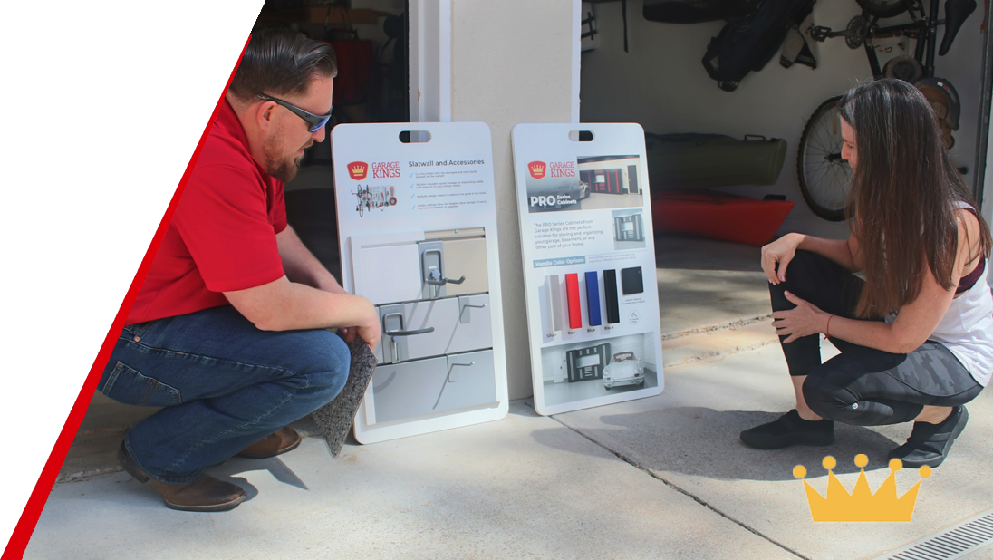 A man and a woman crouch on a driveway, looking at two display boards with garage storage solutions. Garage Kings works closely with their clients to create the best solutions.