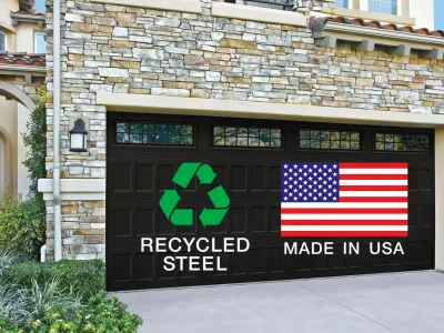 A garage with stone façade features two large black doors each displaying different logos. The left door shows a green recycling symbol with the text "RECYCLED STEEL" underneath, and the right door displays the American flag with the text "MADE IN USA.